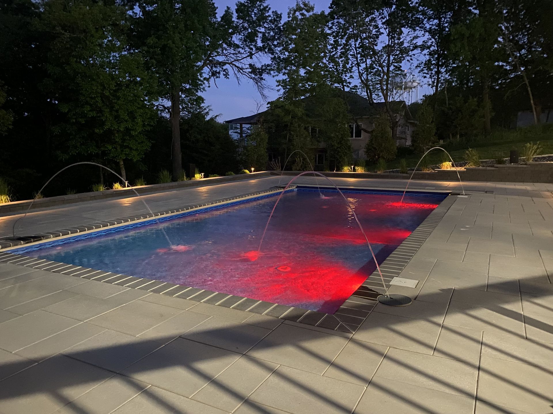 Lit outdoor swimming pool at dusk with red underwater lights and surrounding trees