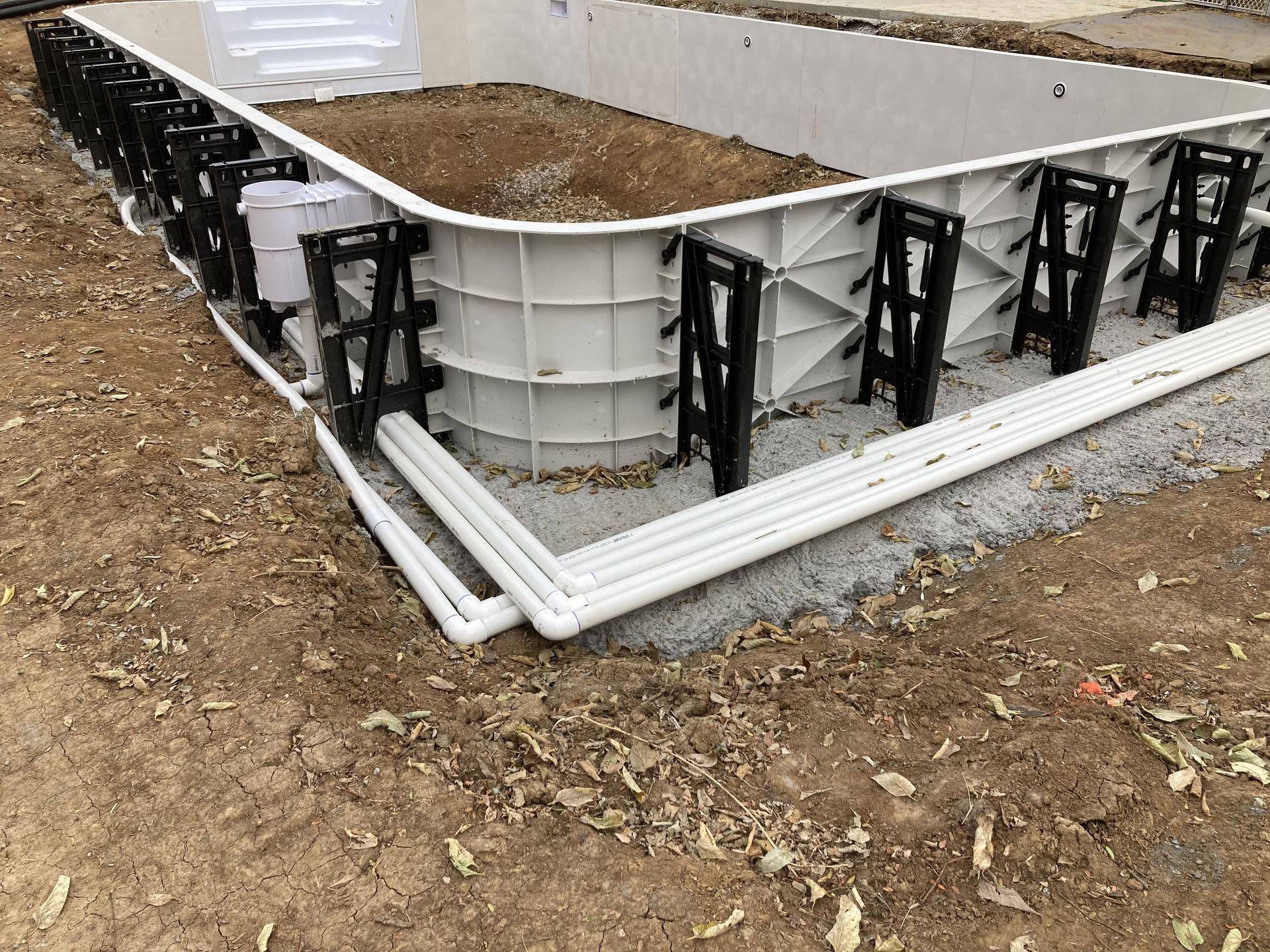 White plastic raised garden bed filled with soil, framed by black brackets on a gravel lot