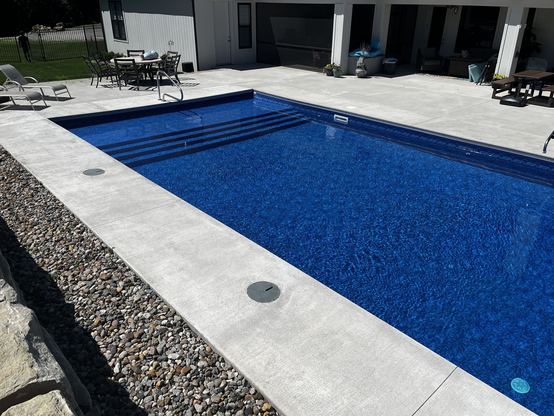 Backyard swimming pool with blue water, white deck, and stone edging beside a patio house