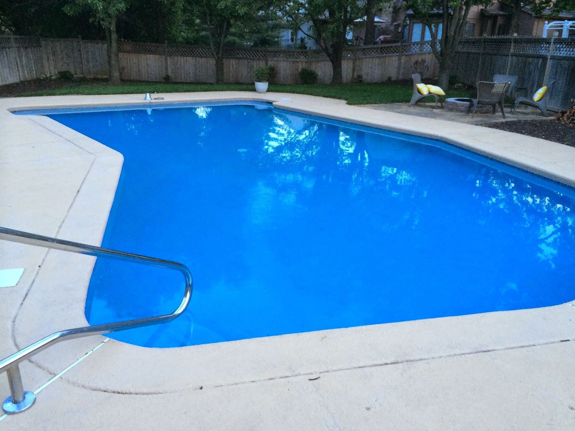 Outdoor swimming pool with bright blue water, concrete deck, and metal handrail in the foreground