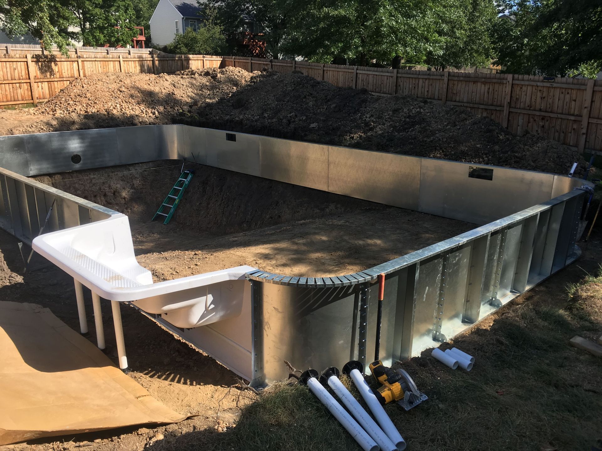 Empty above-ground pool in a backyard, with tools and materials around the partially assembled walls.