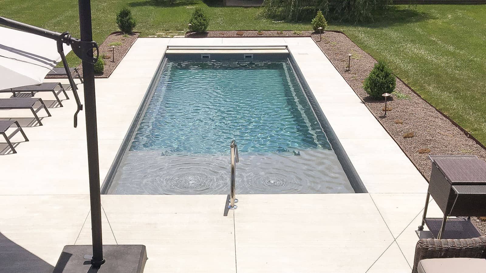 Rectangular backyard pool with white deck, green lawn, and lounge chairs in bright daylight