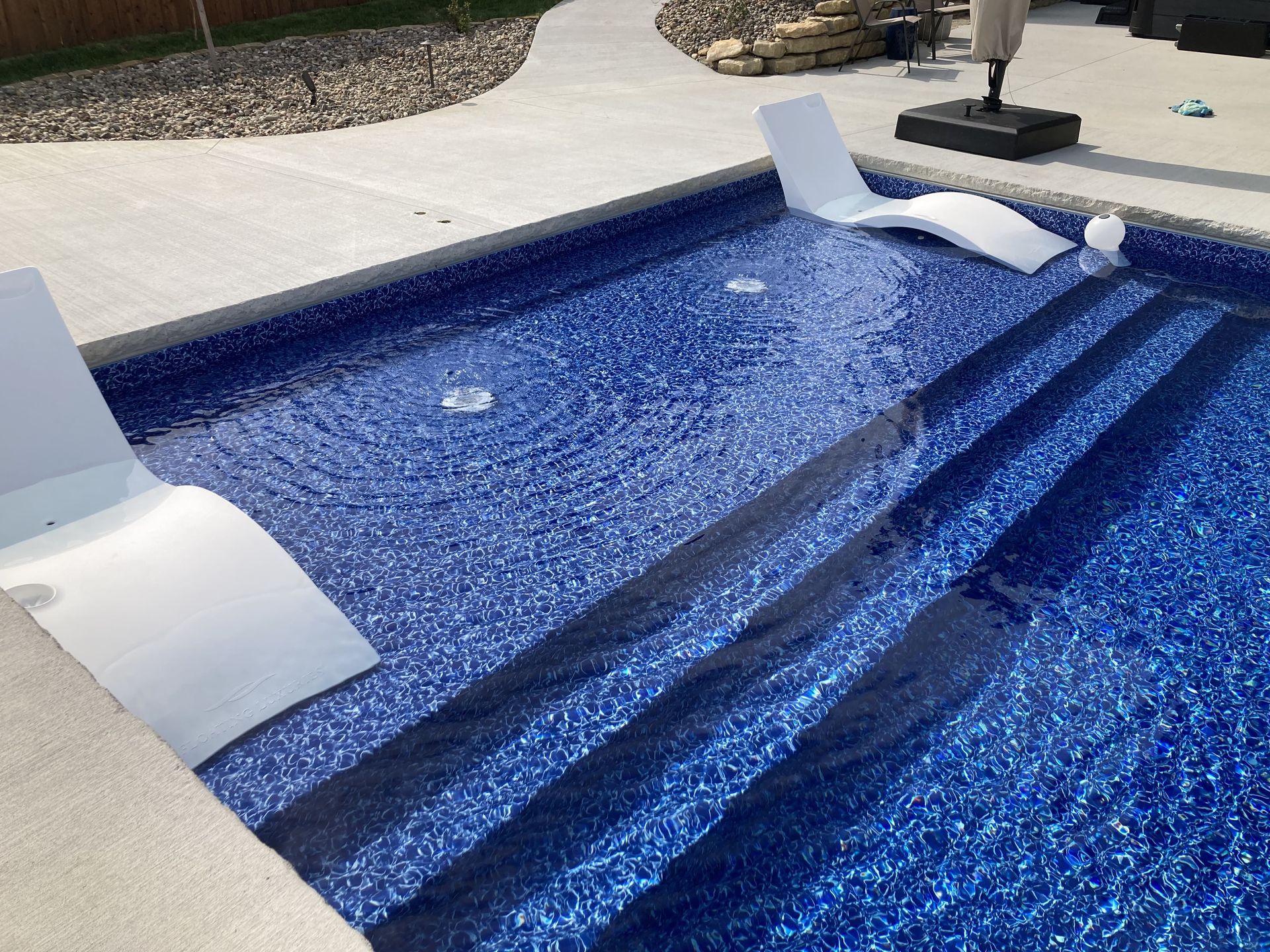 Backyard swimming pool with blue mosaic tile steps and white lounge chairs at the shallow end