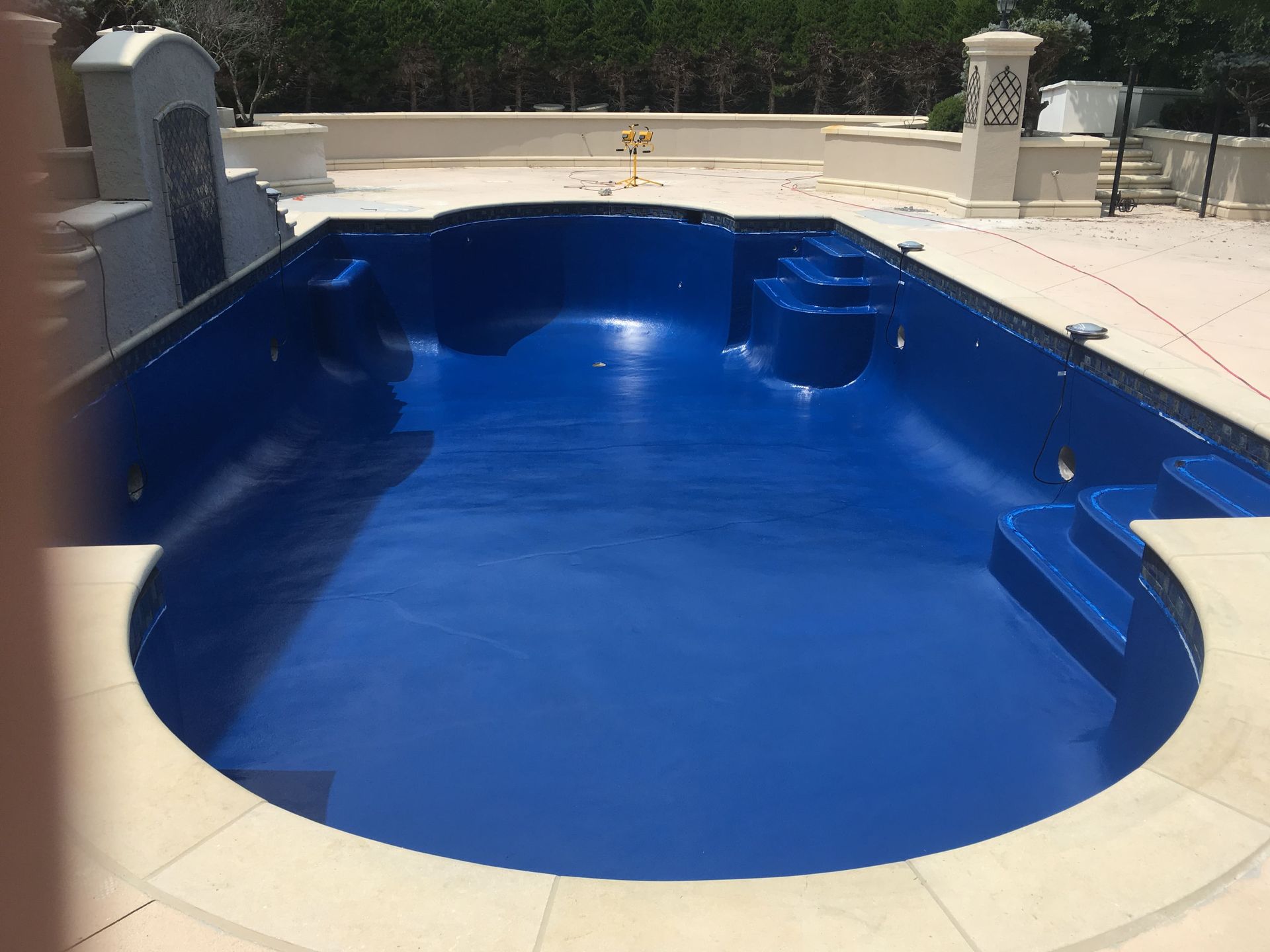 Empty blue backyard swimming pool with beige deck and stone coping in bright sunlight