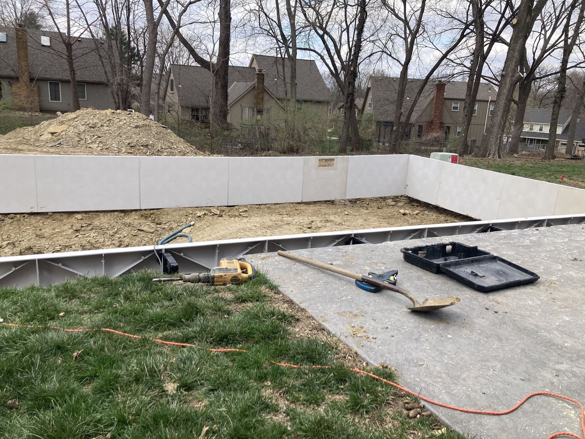 Backyard concrete patio under construction with tools, forms, and a white retaining wall behind it