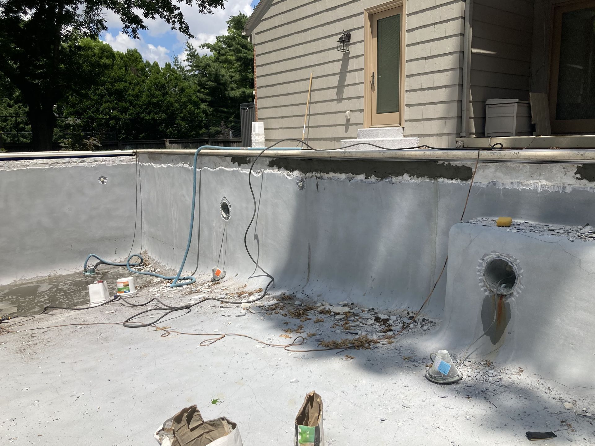 Empty concrete pool with peeling walls and debris beside a house