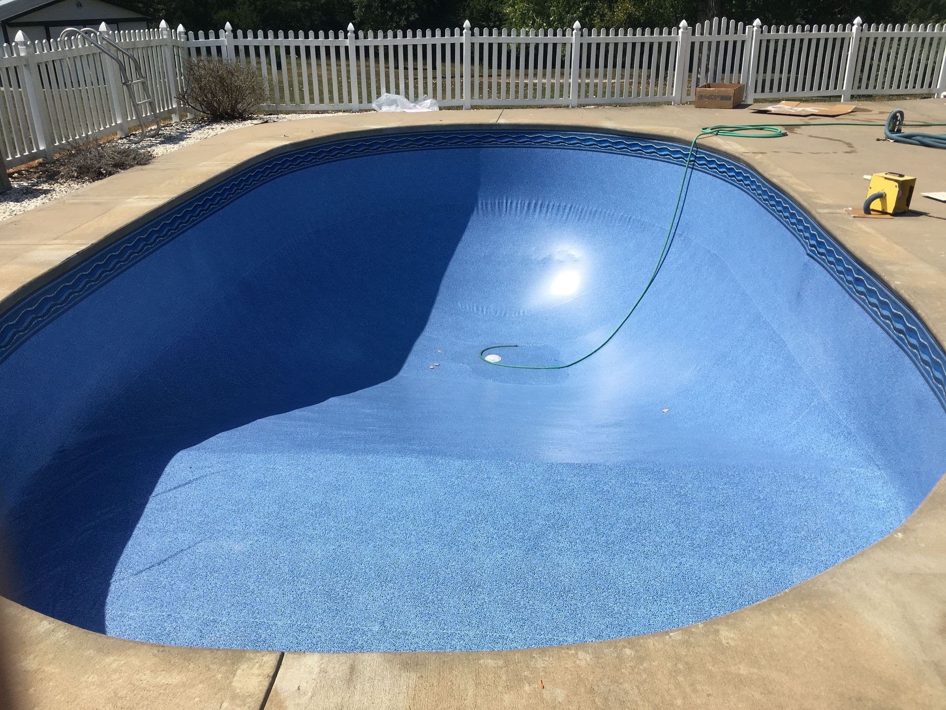 Empty blue swimming pool under construction in a fenced backyard