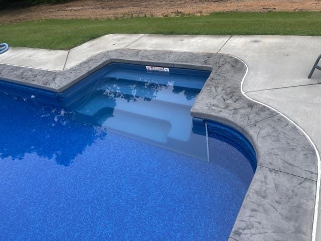 Blue swimming pool with curved concrete edge and shallow steps