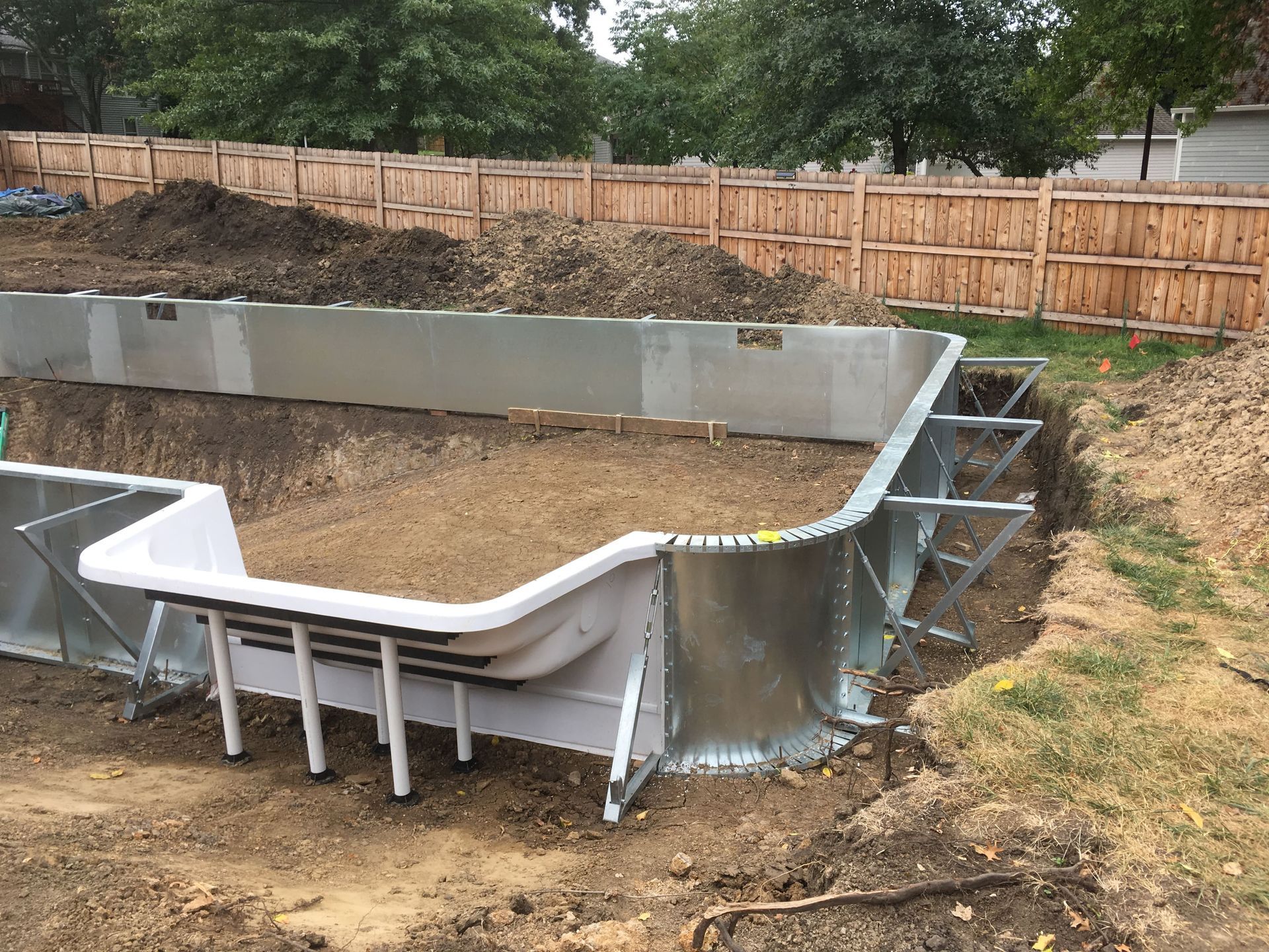 Partially built above-ground pool in a backyard, surrounded by dirt and a wooden fence.