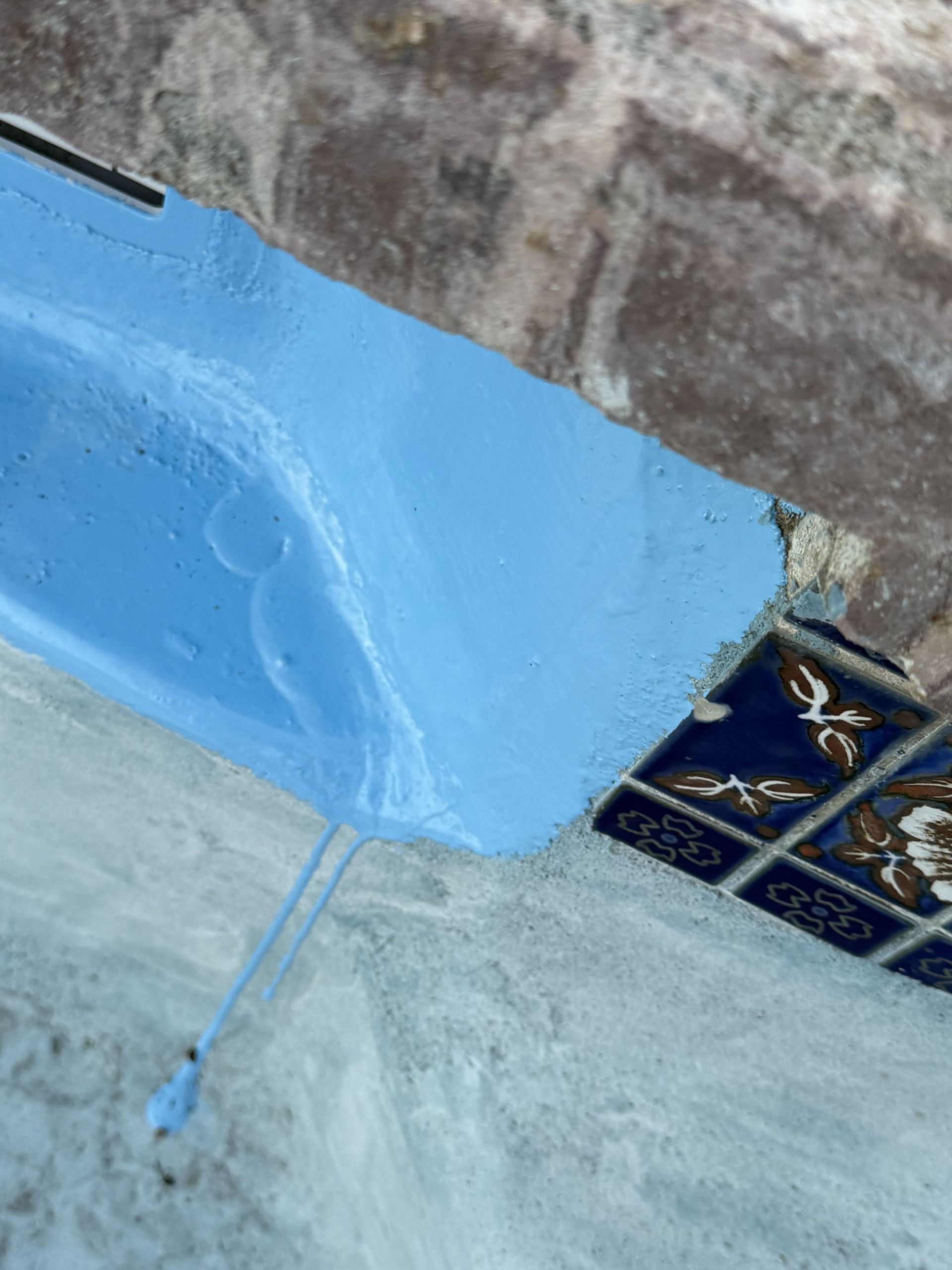 Blue painted corner with a drip mark next to a tiled floor and rough gray surface