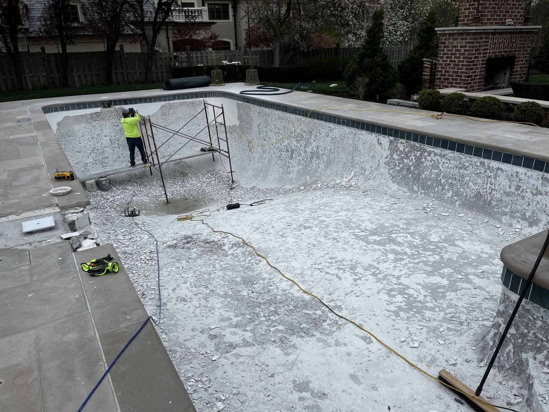 Empty drained swimming pool being resurfaced, with a worker in a neon vest near the far end.