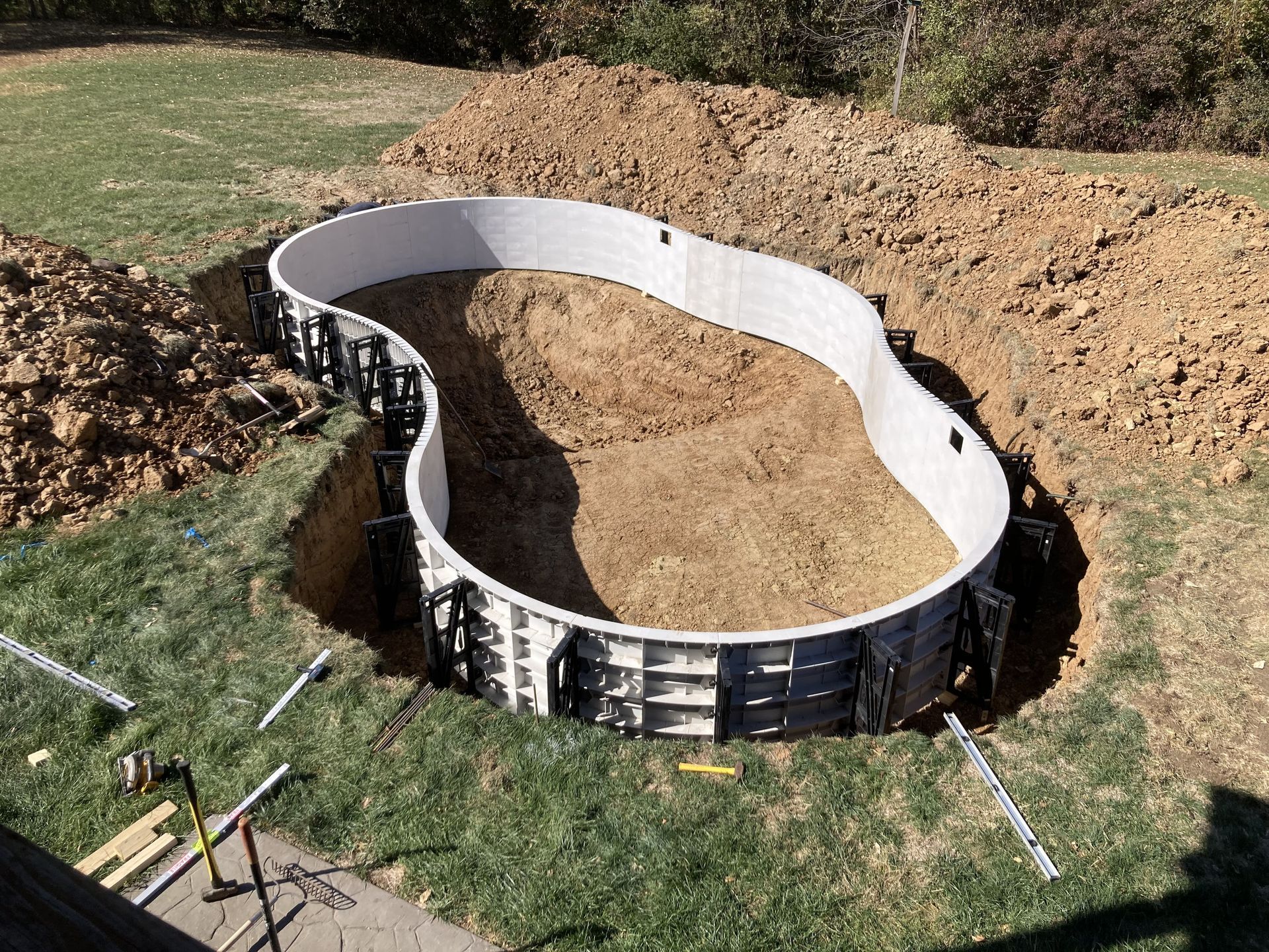 Curved black retaining wall outlining a newly dug backyard pond or garden bed with dirt inside