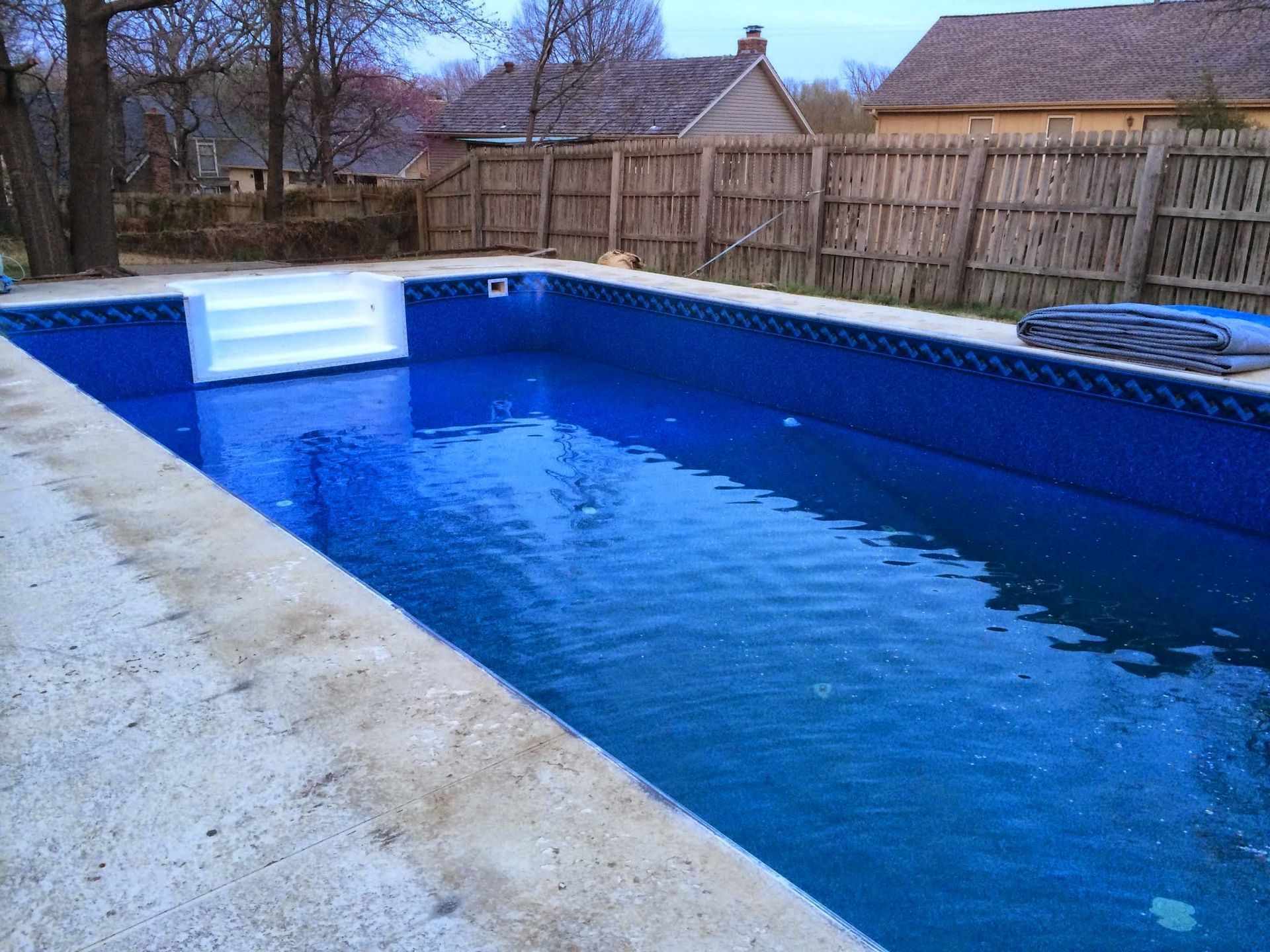 Empty blue swimming pool with tiled walls and a wooden fence in a backyard