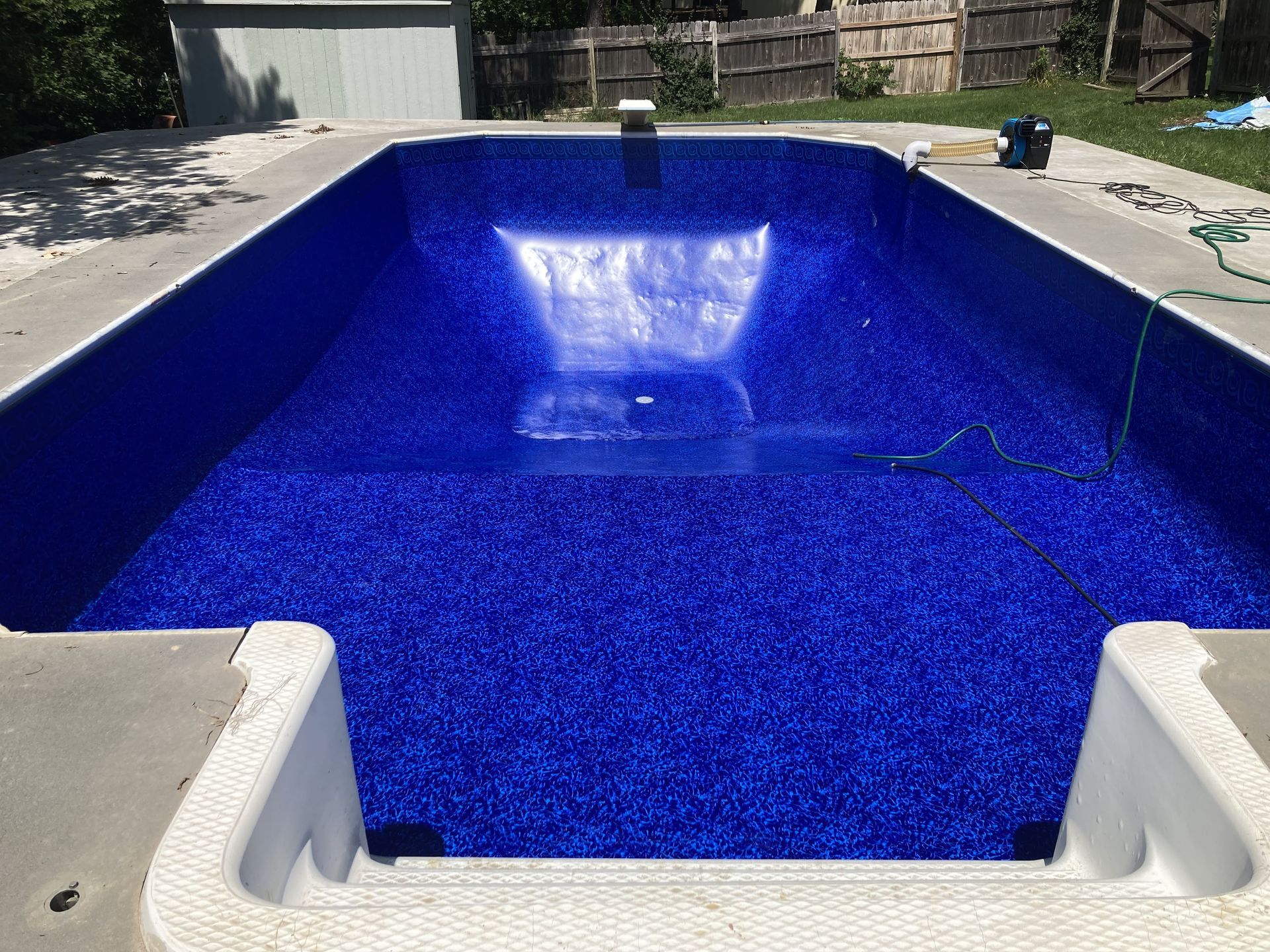 Empty blue-lined swimming pool with concrete deck and steps, outdoors in a backyard