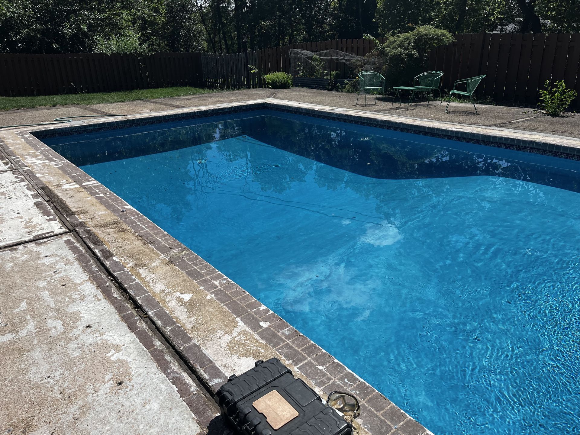 Blue backyard swimming pool with stone deck and bright sunlight