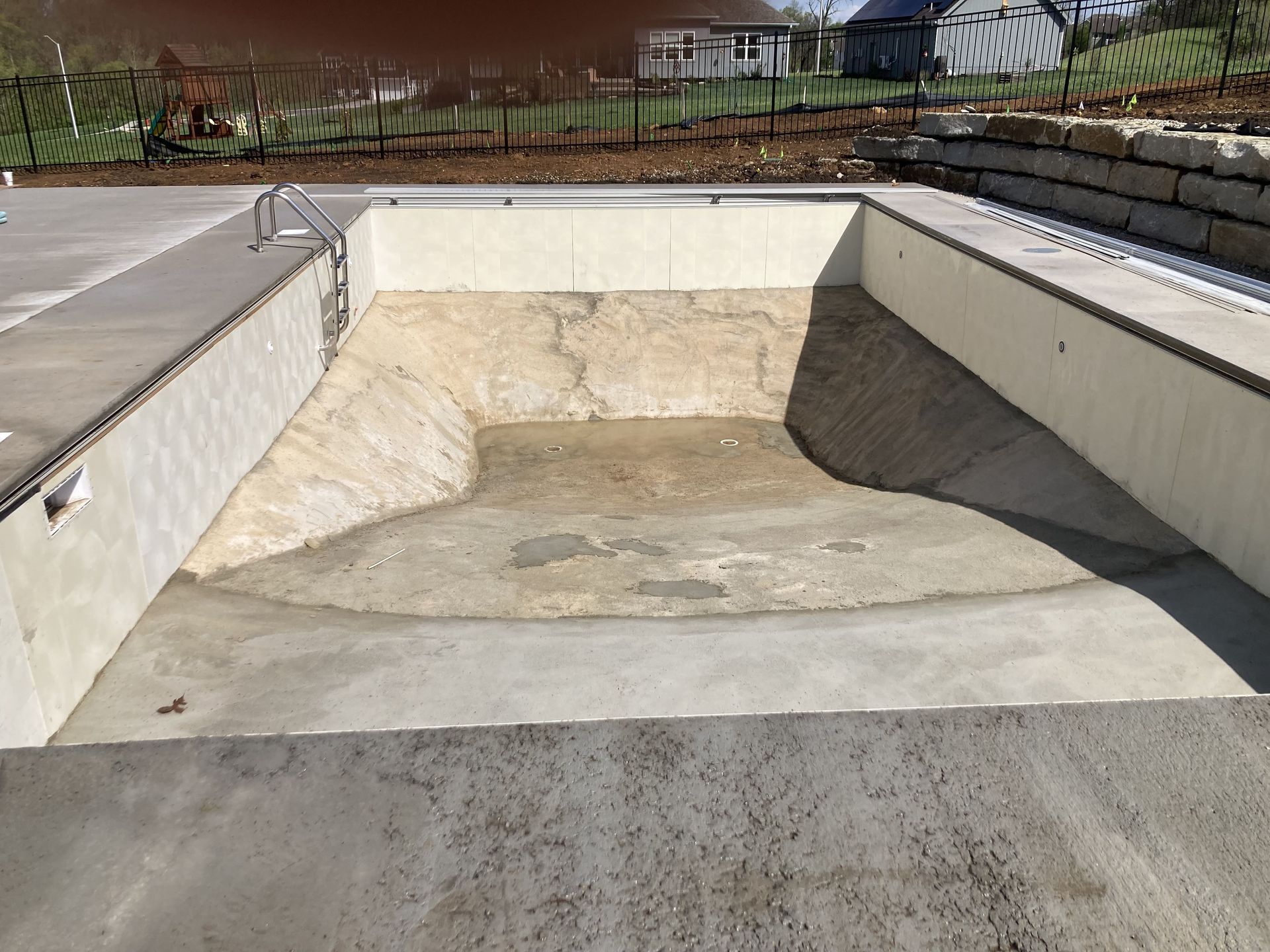 Empty concrete swimming pool under construction outdoors, with surrounding deck and fence.