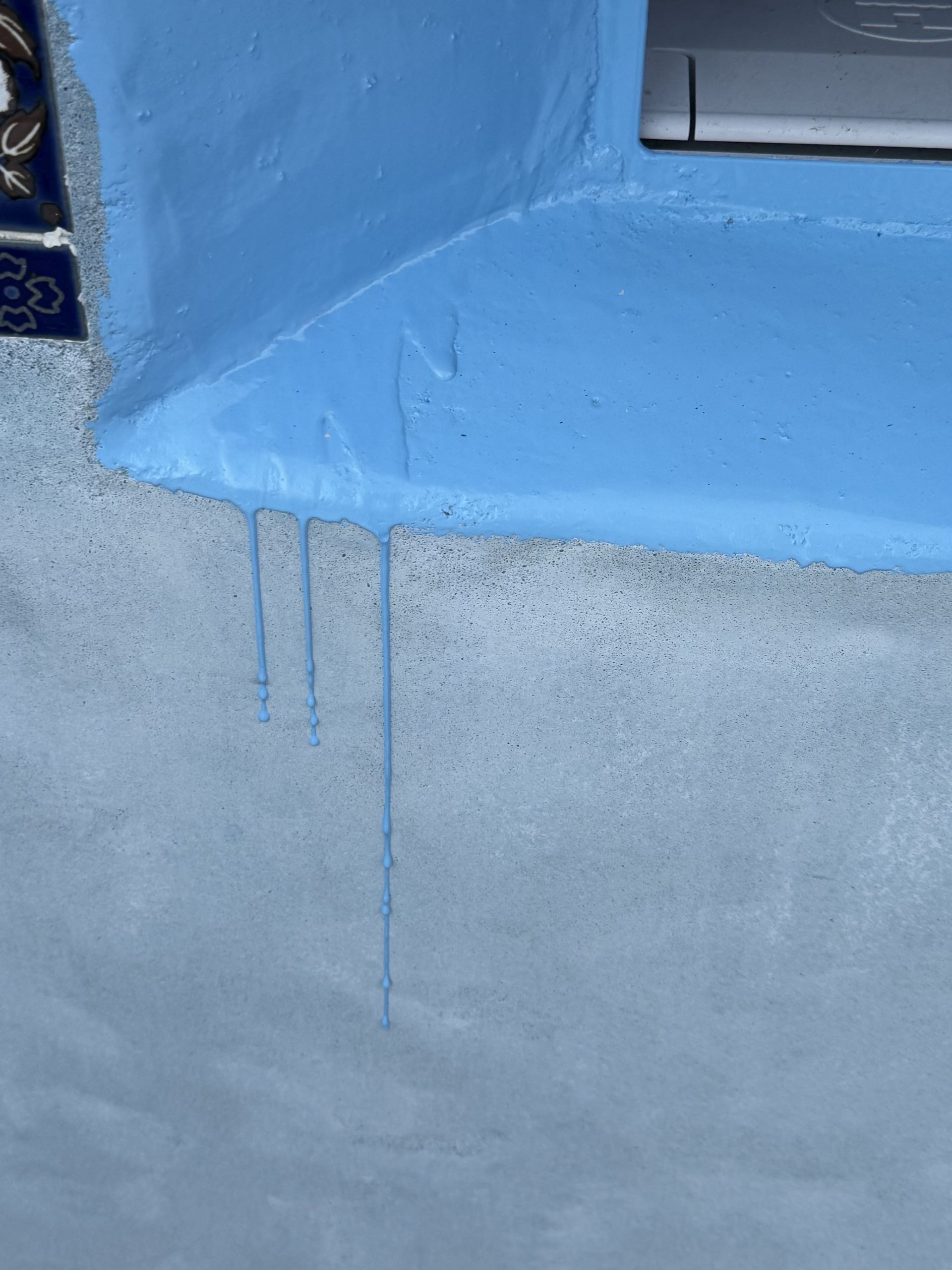 Blue paint drips down a light gray wall beneath a blue ledge.