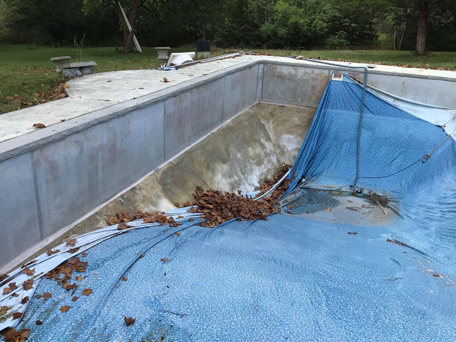 Empty abandoned pool with blue tarp and scattered leaves, viewed from the corner