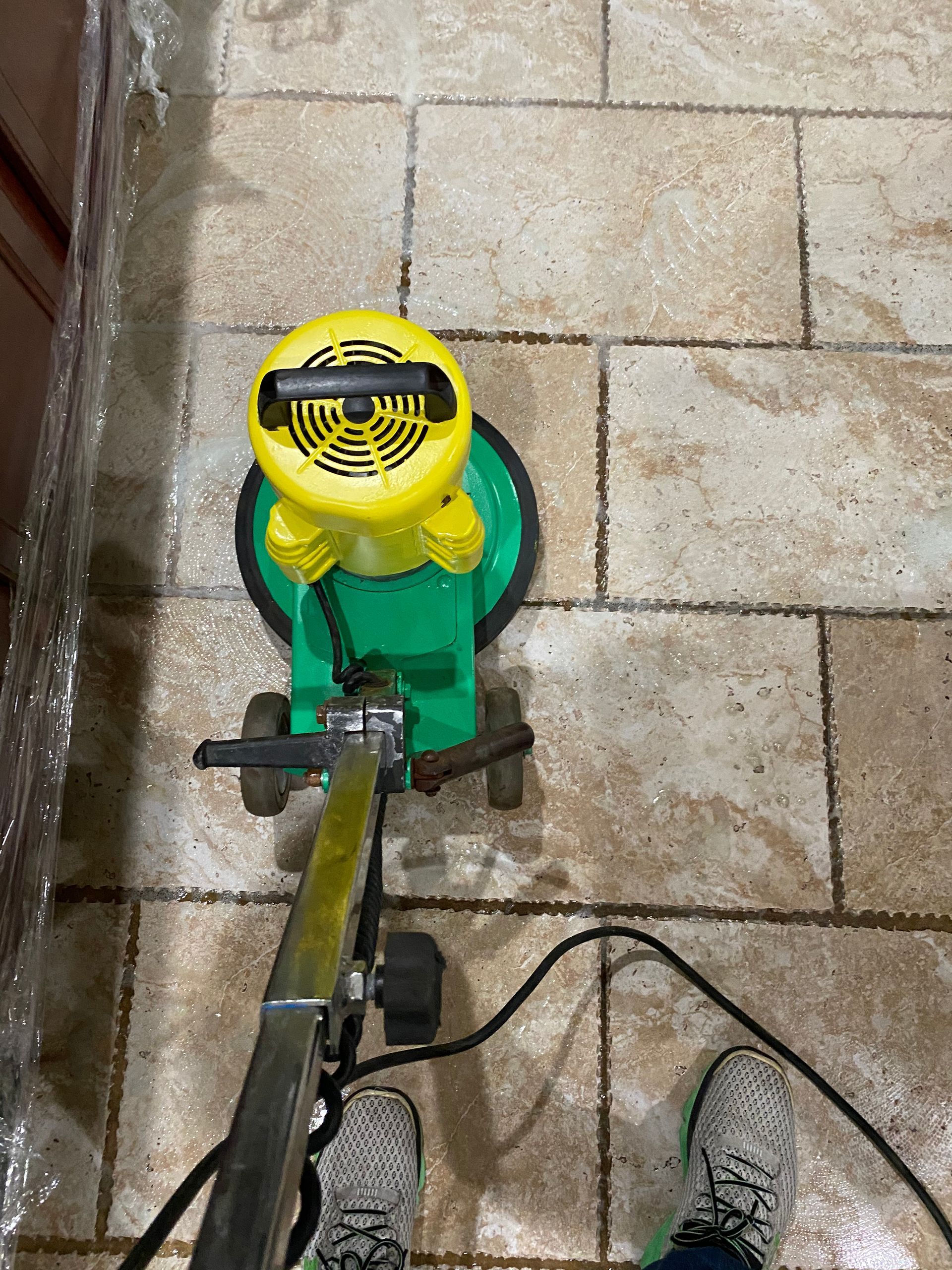 A person using a green and yellow floor cleaning machine on tiled floor.