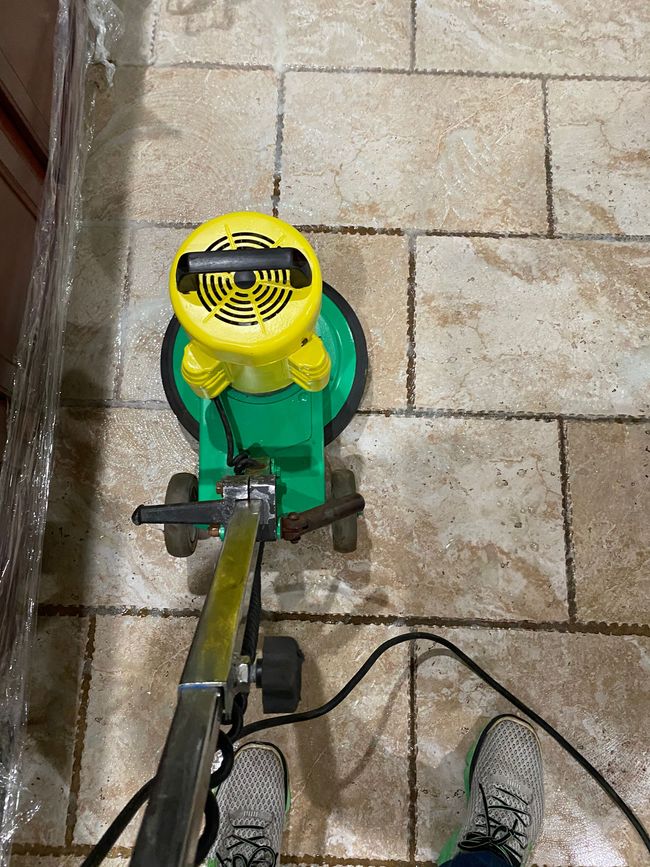 A person using a green and yellow floor cleaning machine on tiled floor.