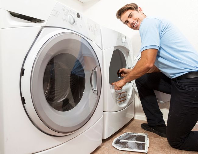Man inspecting lint trap of a dryer in a laundry room, smiling.