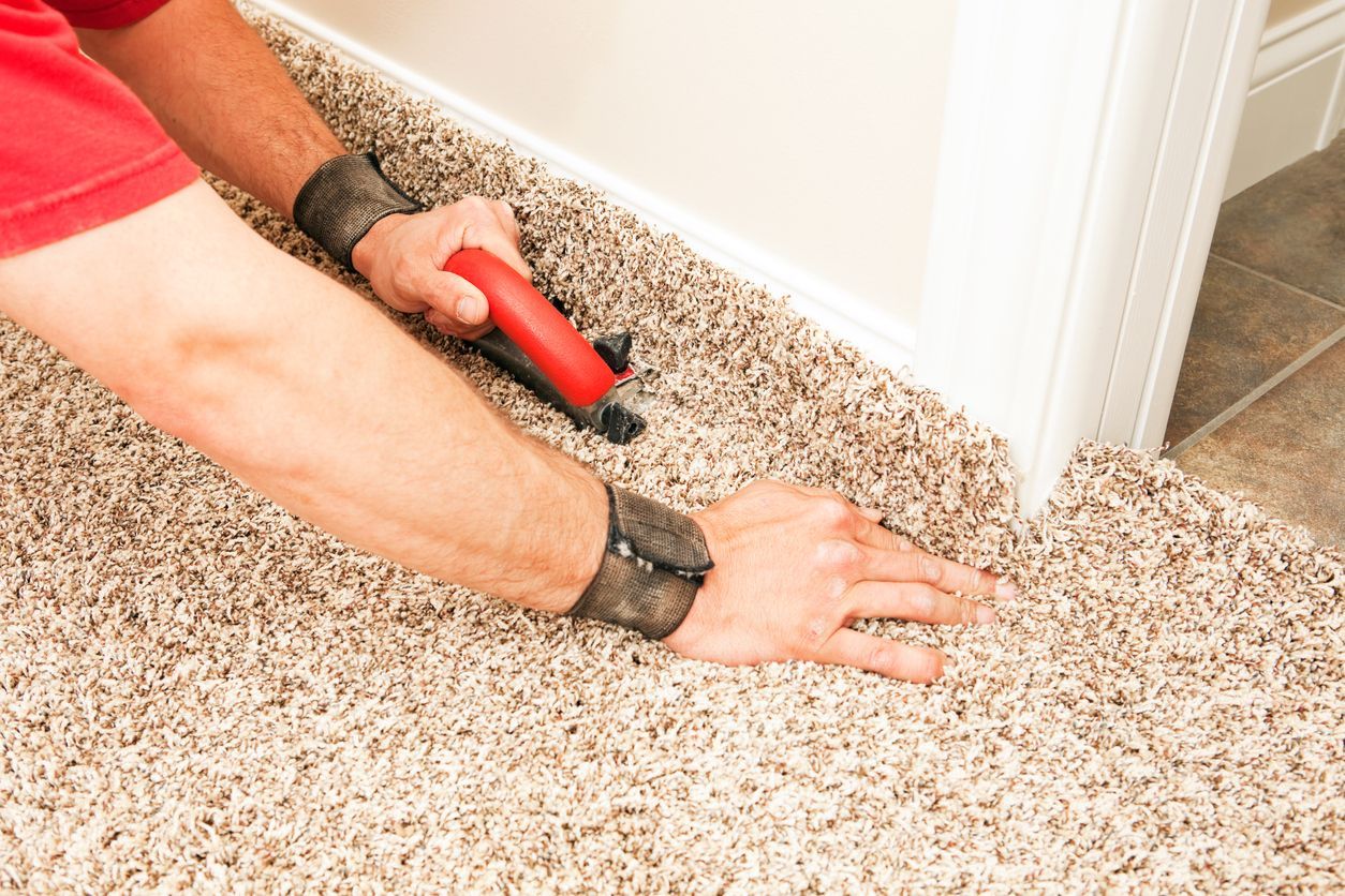 Person installing carpet, using a tool to trim it along a white wall.