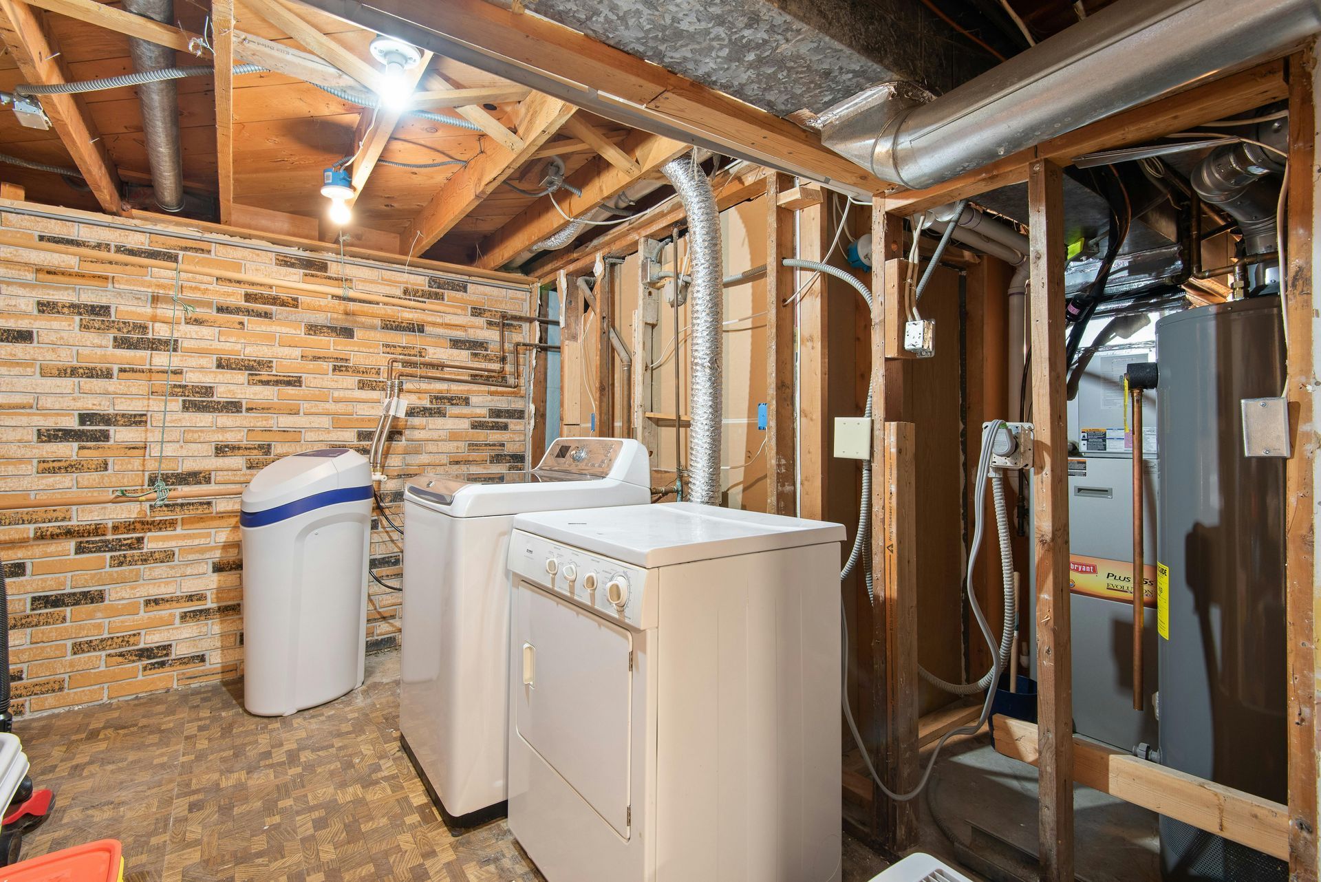 Laundry room with washer and dryer, exposed ceiling beams, brick wall, and water heater machinery