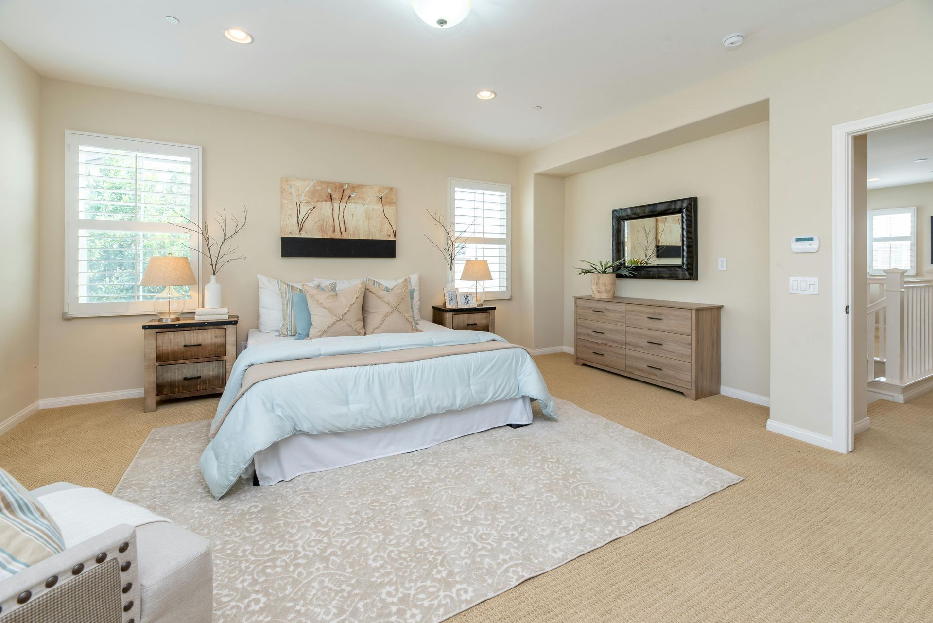 Bedroom with light walls, large bed, light blue bedding, two nightstands, and a light-colored rug.
