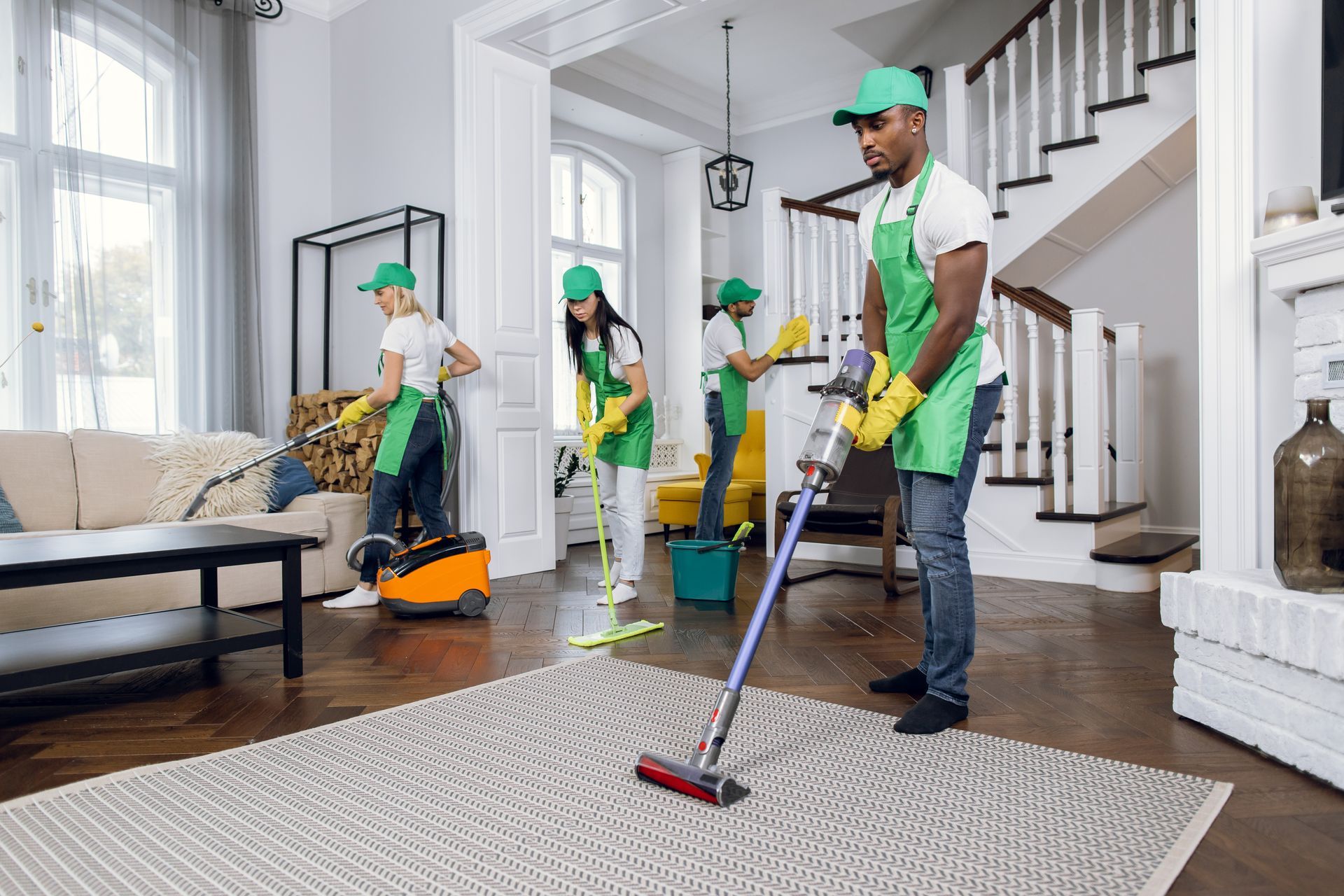 Person vacuuming a gray sofa with a handheld attachment indoors.