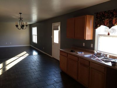 Empty kitchen with dark tile floor, wood cabinets, sink, window, and sunlight across the room