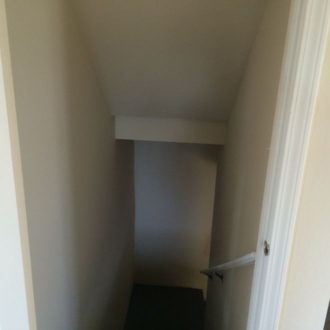 Narrow beige stairwell descending to a dark lower landing with a white handrail on the right