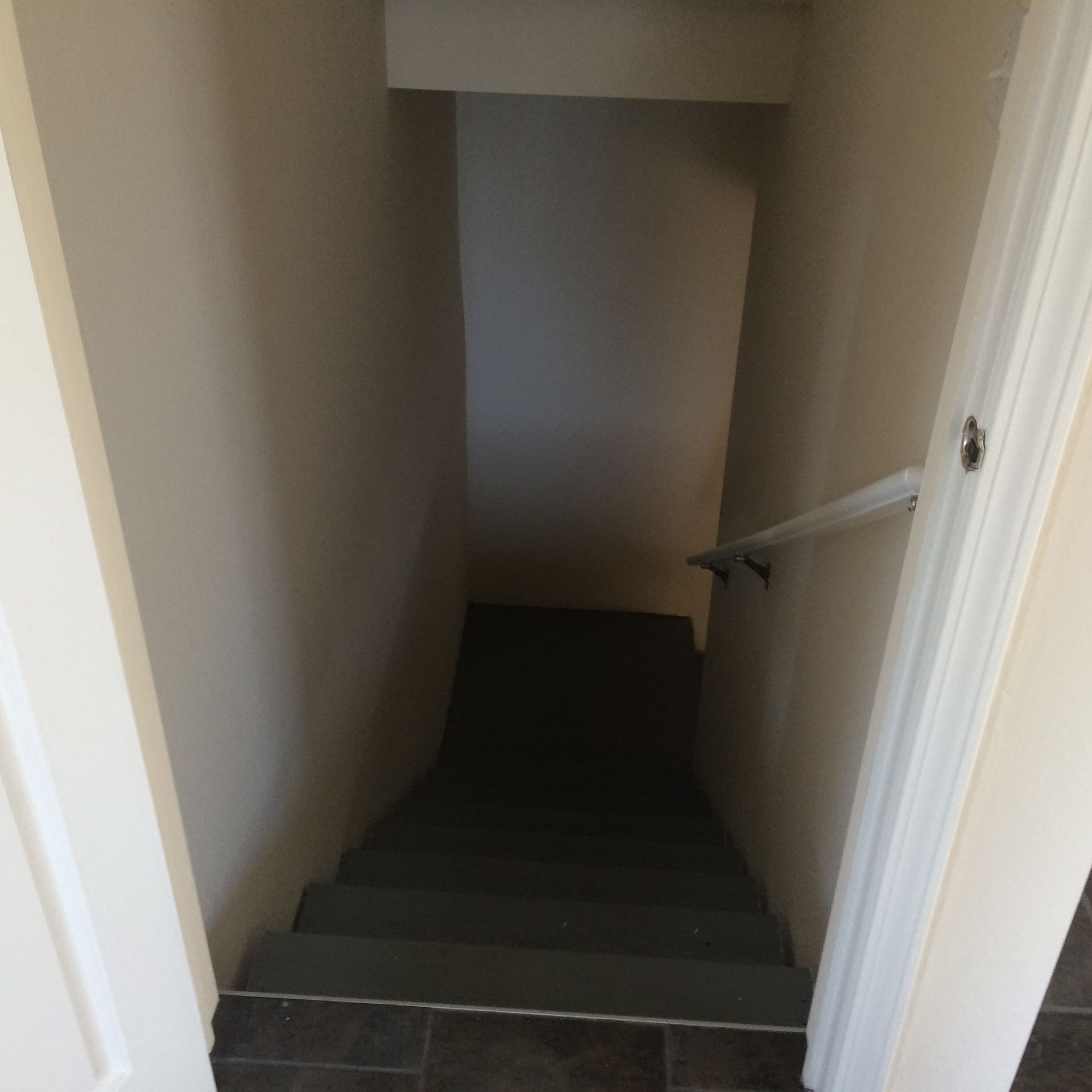 Narrow beige stairwell with dark steps descending to a dim lower landing.