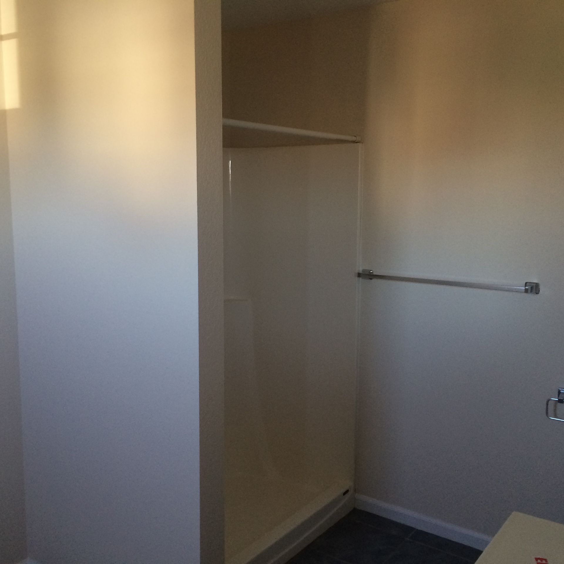 Empty closet with a white shelf and hanging rod in a beige room.