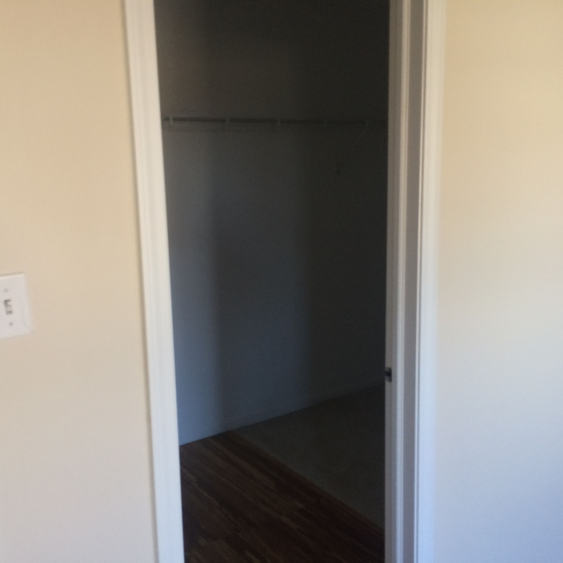 Open closet doorway in a beige room with white trim and dark wood flooring
