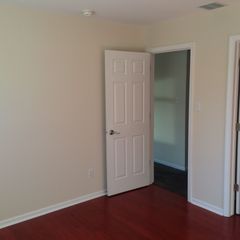 Empty room with beige walls, red hardwood floor, and an open white door to a hallway