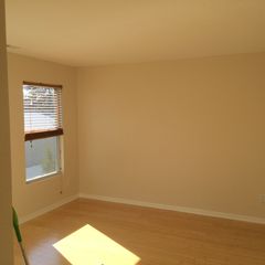 Empty beige room with hardwood floor and a small window with blinds letting in sunlight