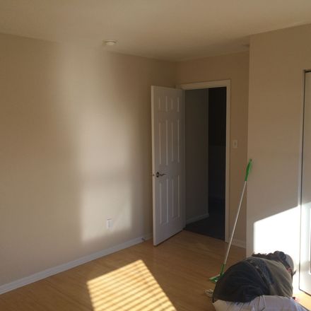 Empty beige room with wood floor, open white door, and broom near sunlight on the floor.