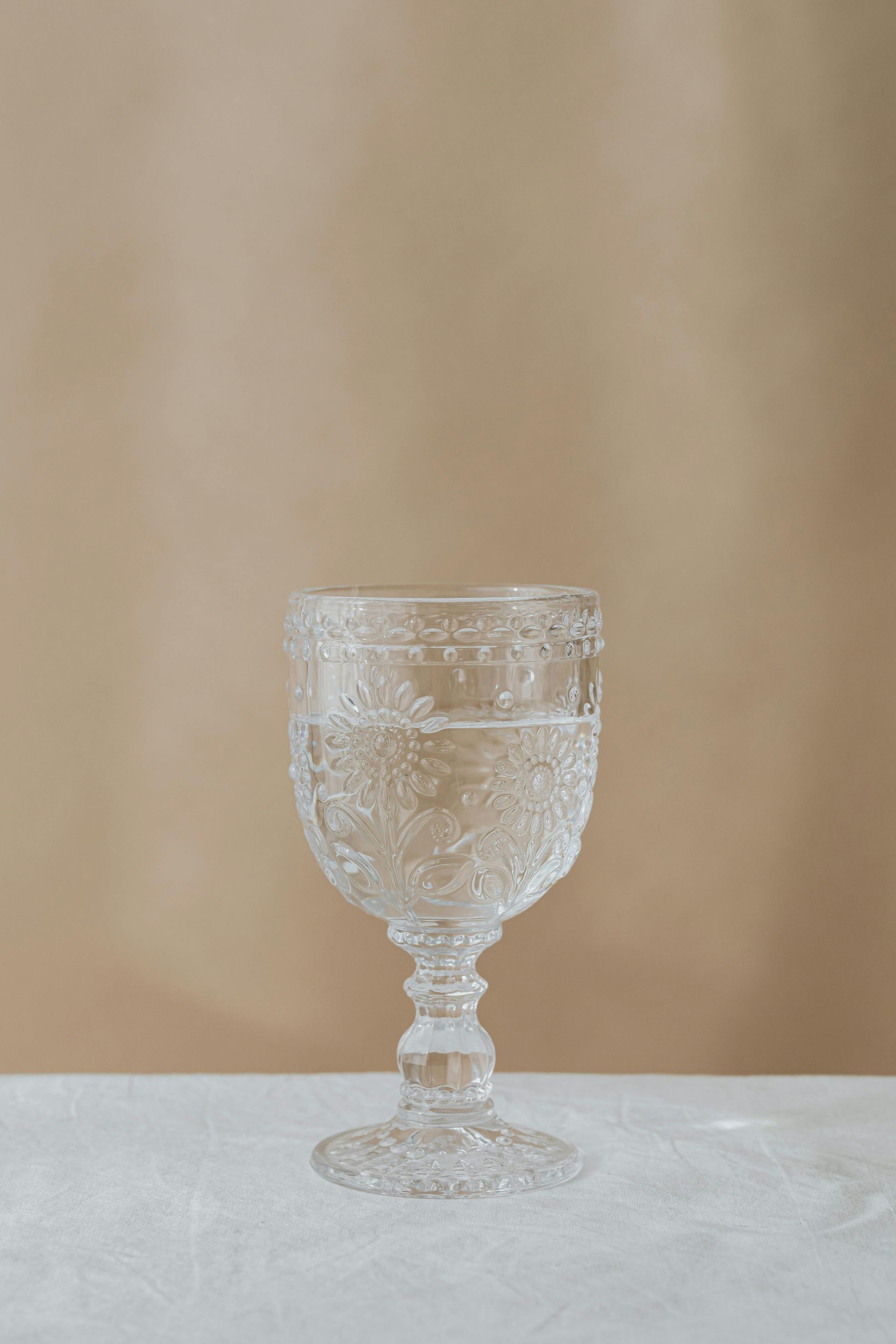 Helder, sierlijk glas gevuld met vloeistof, staand op een witte ondergrond tegen een beige achtergrond.