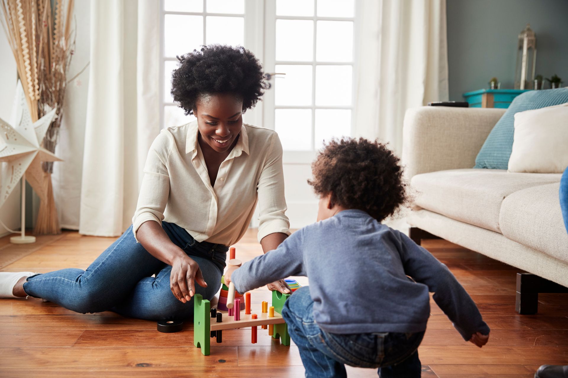 Woman and child playing with a colorful toy on a wooden floor in a living room.