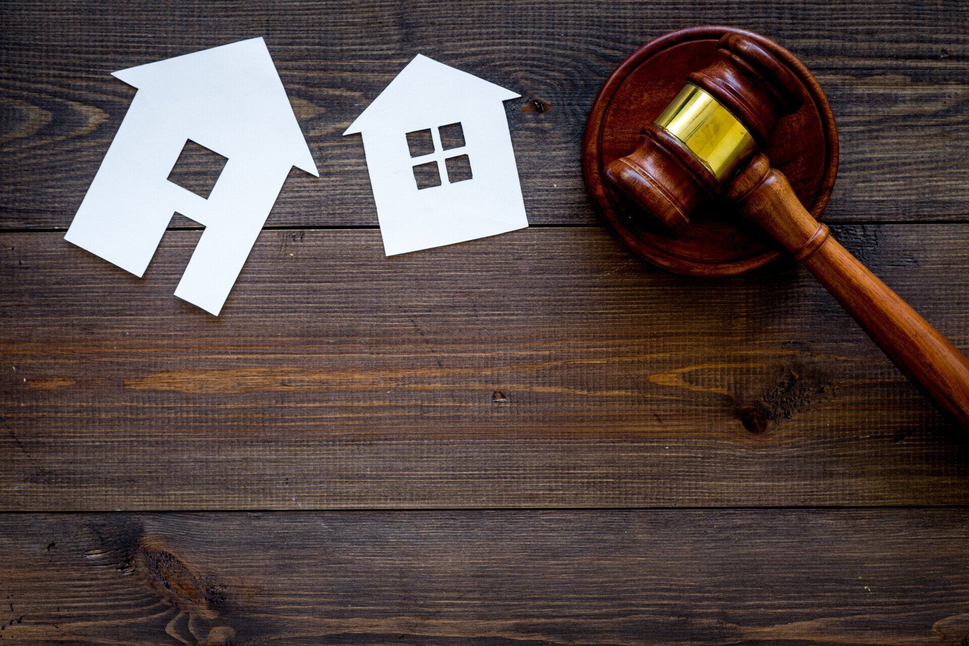 A wooden gavel is sitting on a wooden table next to paper houses.