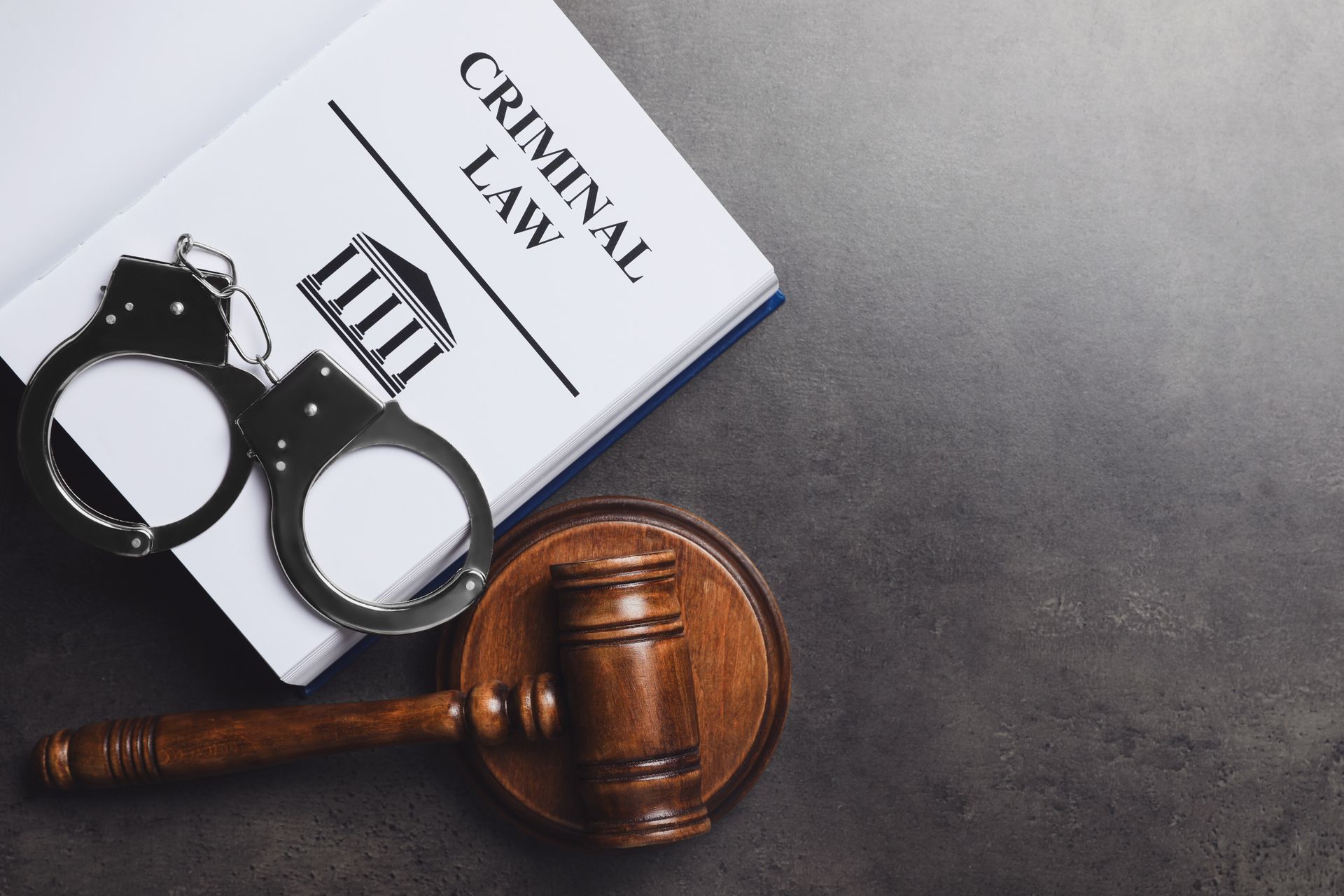 A book on criminal law with handcuffs and a judge 's gavel on a table.