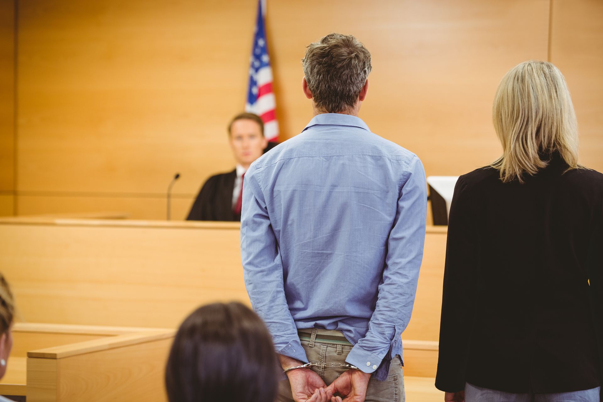 A man in court wearing handcuffs and standing next to his attorney.