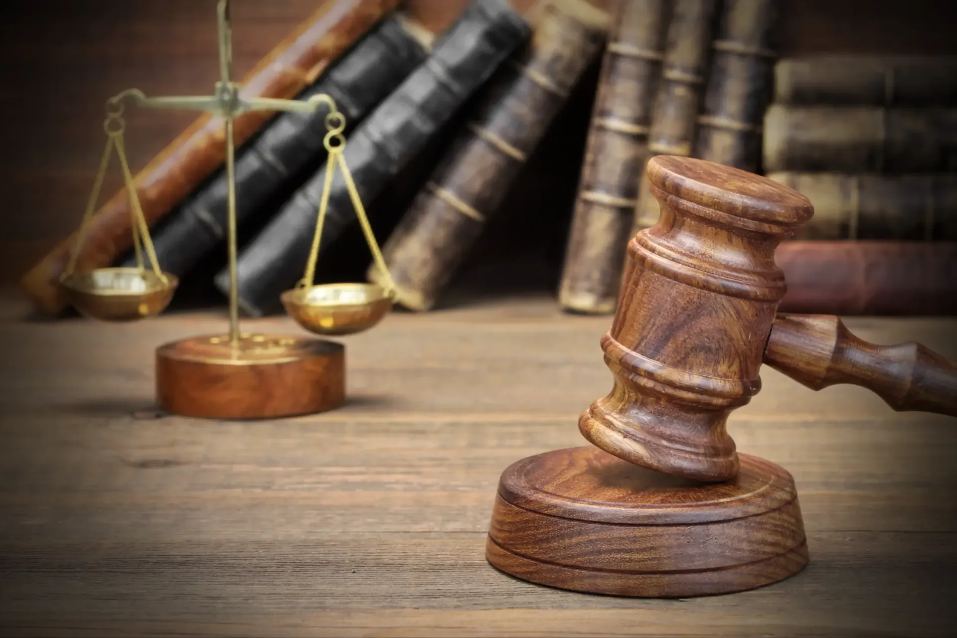 A wooden judge's gavel and scales of justice on a wooden table.