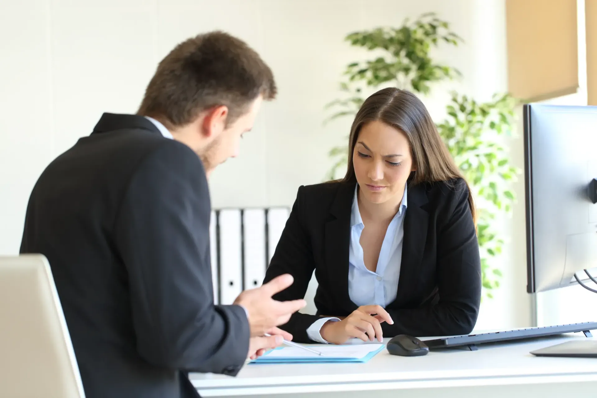 A man and a woman are sitting at a desk having a conversation.