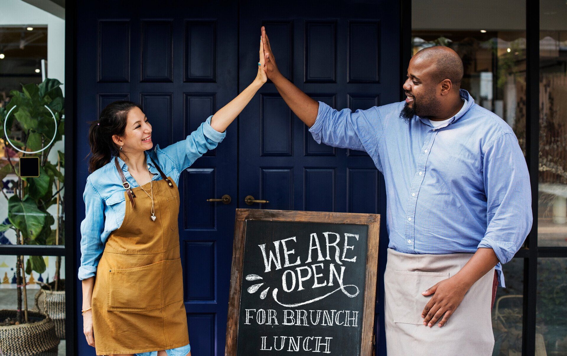 A man and a woman are giving each other a high five in front of a restaurant.