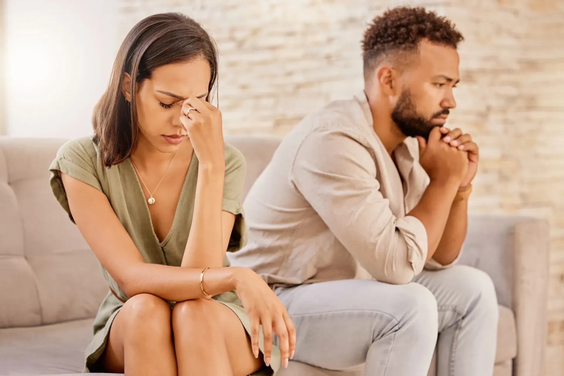 Woman and man sitting apart on a couch, appearing distressed; woman holding her forehead.