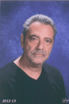 Man in black shirt against a blue background, with short gray hair and a serious expression.
