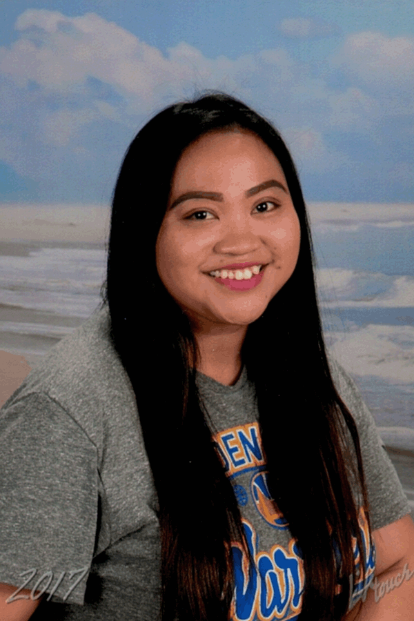 Woman with long black hair, smiling, wearing a gray shirt, in front of a beach background.