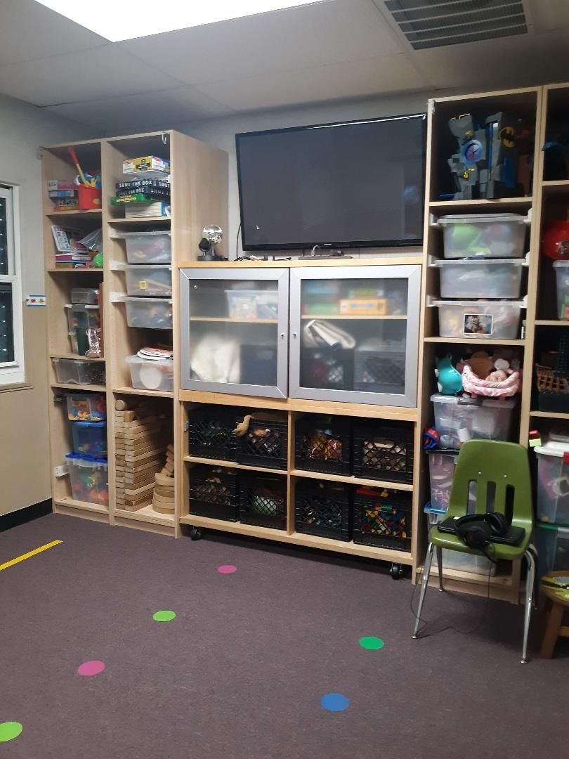 Shelving unit filled with toys and supplies, a TV, and a green chair in a playroom setting.