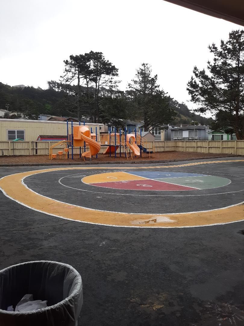 Playground with orange slides, surrounded by a colorful, circular paved area, under an overcast sky.